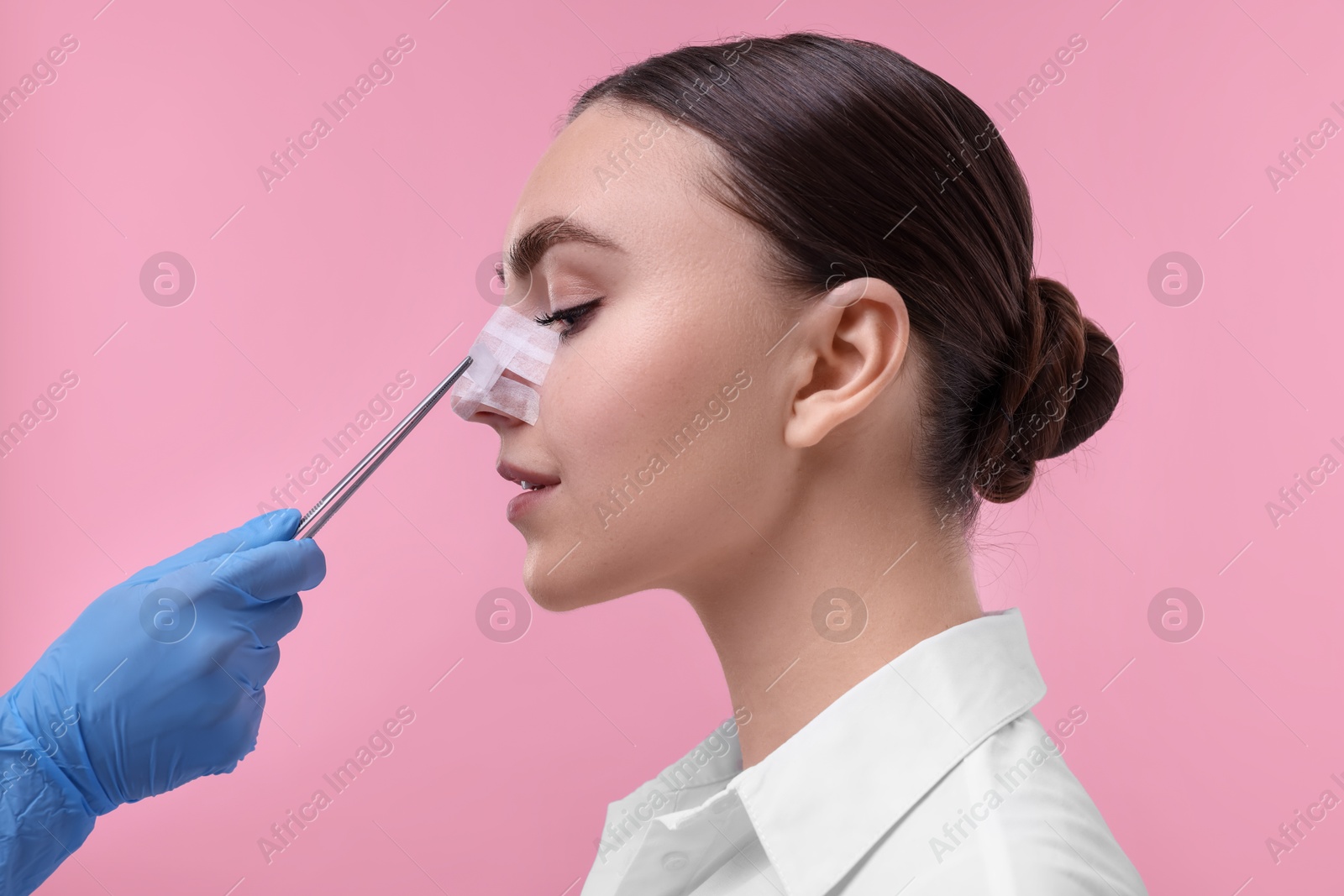 Photo of Doctor removing medical bandage from patient's nose after plastic surgery operation on pink background, closeup