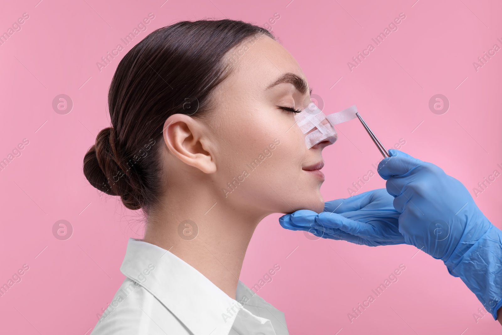 Photo of Doctor removing medical bandage from patient's nose after plastic surgery operation on pink background, closeup