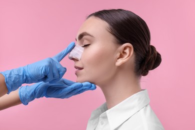 Photo of Doctor checking patient's nose after plastic surgery operation on pink background, closeup