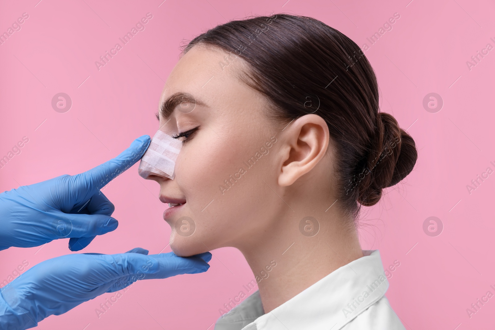 Photo of Doctor checking patient's nose after plastic surgery operation on pink background, closeup