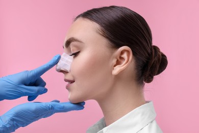 Doctor checking patient's nose after plastic surgery operation on pink background, closeup