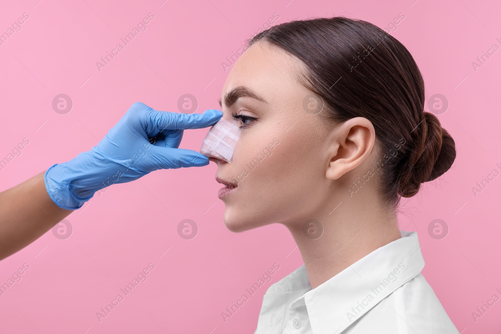 Photo of Doctor checking patient's nose after plastic surgery operation on pink background, closeup