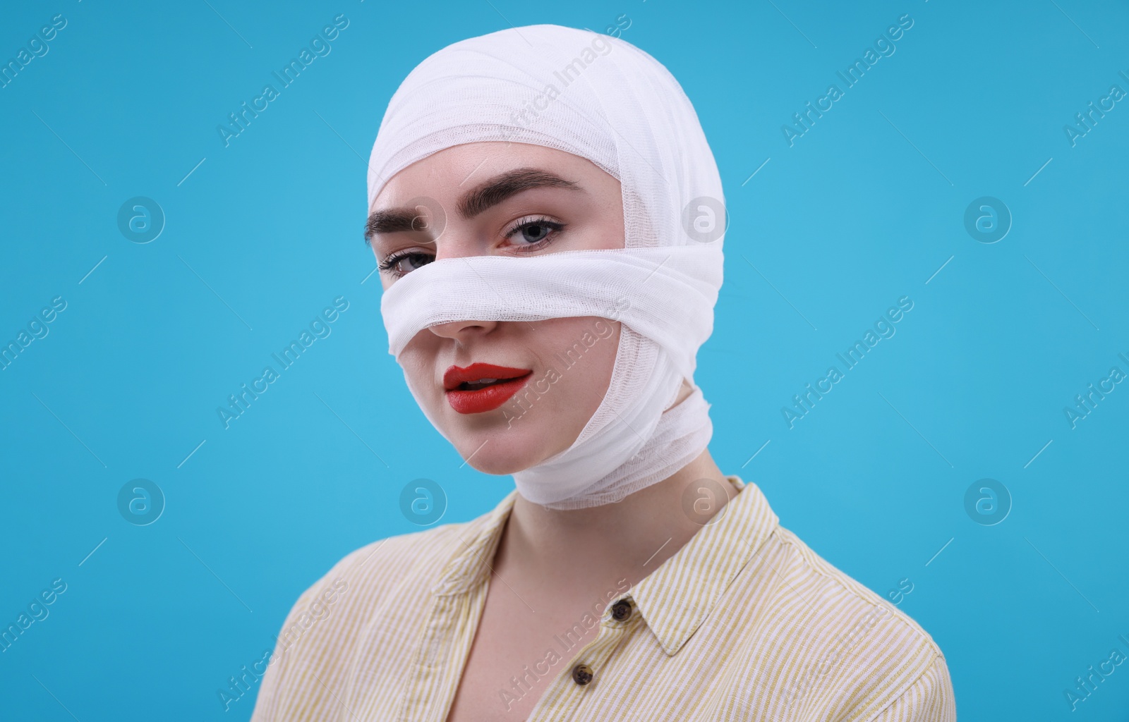 Photo of Woman with nose wrapped in medical bandage after plastic surgery operation on light blue background