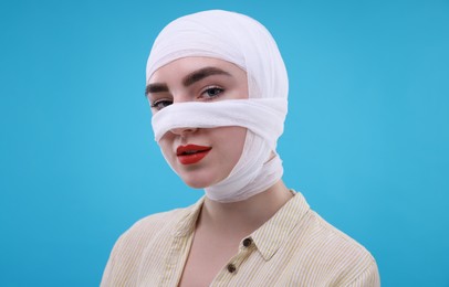 Woman with nose wrapped in medical bandage after plastic surgery operation on light blue background