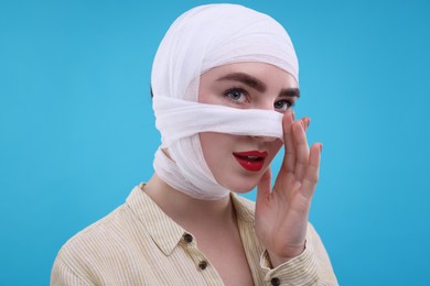 Photo of Woman with nose wrapped in medical bandage after plastic surgery operation on light blue background