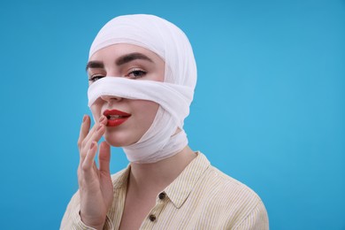 Photo of Woman with nose wrapped in medical bandage after plastic surgery operation on light blue background