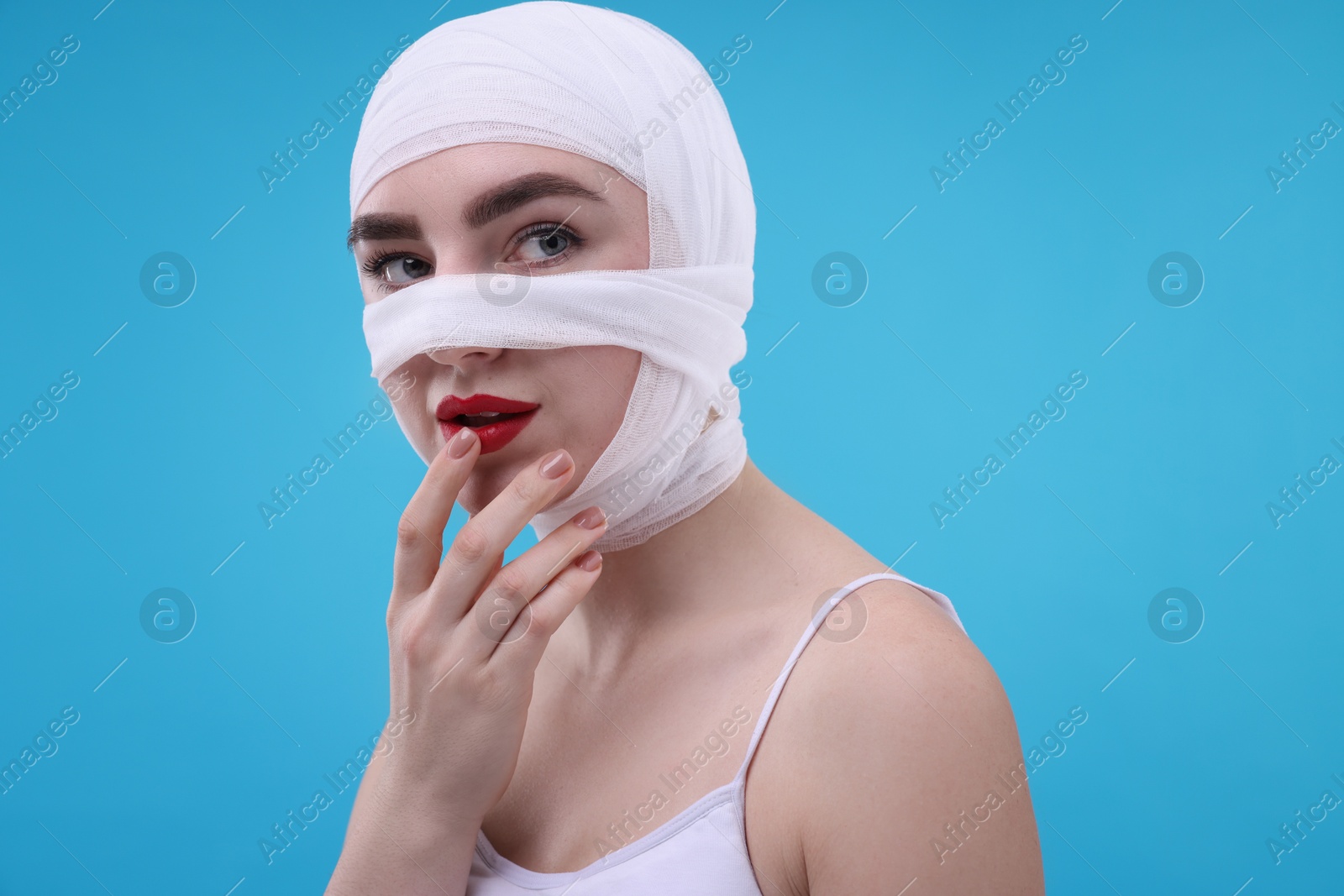 Photo of Woman with nose wrapped in medical bandage after plastic surgery operation on light blue background