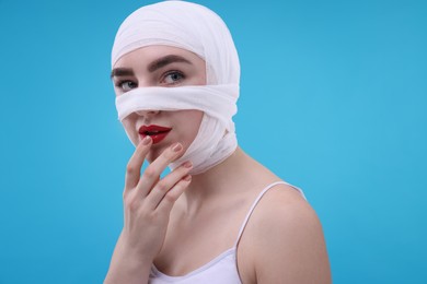 Woman with nose wrapped in medical bandage after plastic surgery operation on light blue background