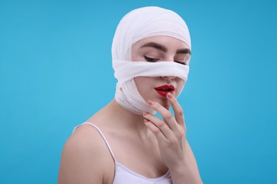 Photo of Woman with nose wrapped in medical bandage after plastic surgery operation on light blue background