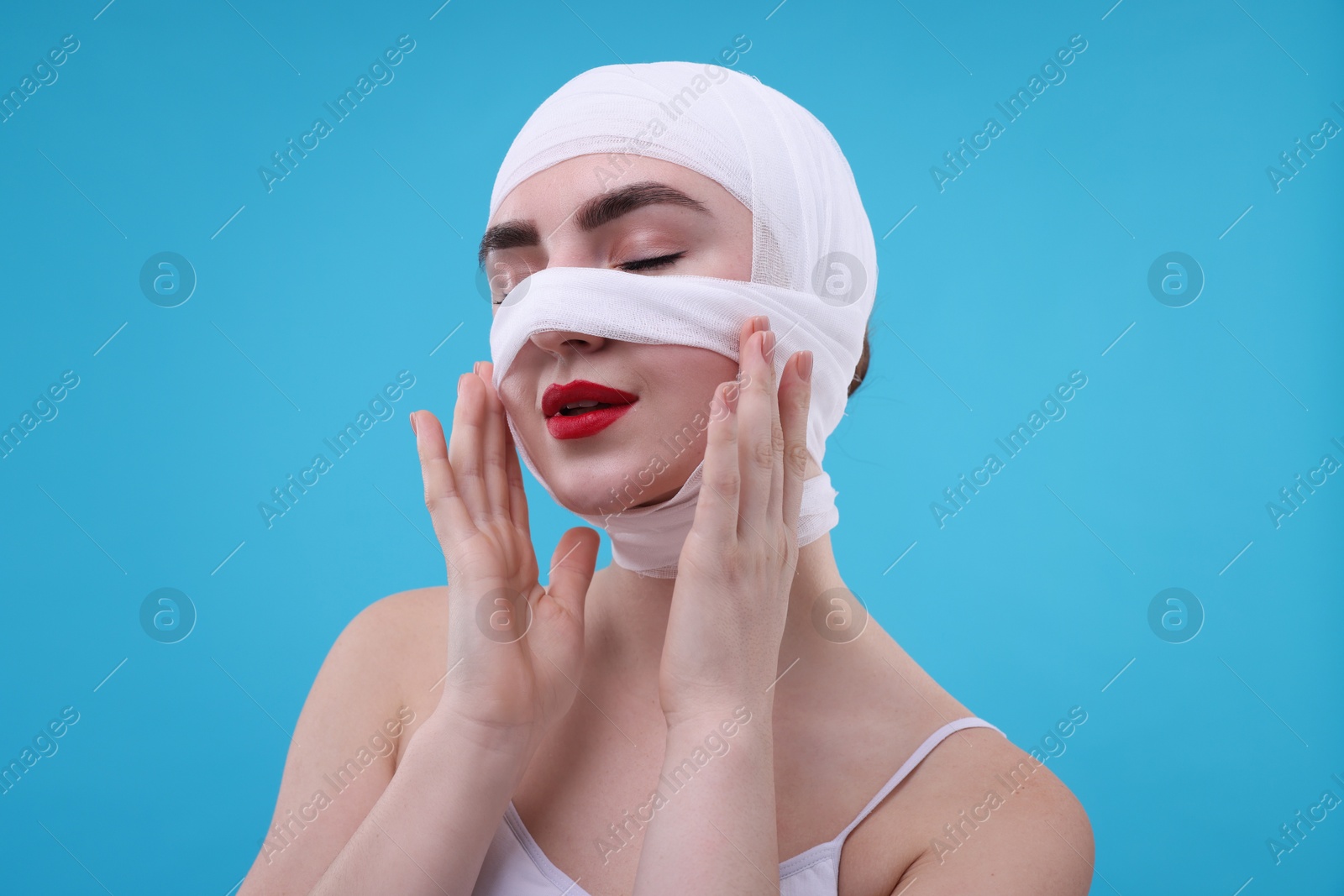 Photo of Woman with nose wrapped in medical bandage after plastic surgery operation on light blue background