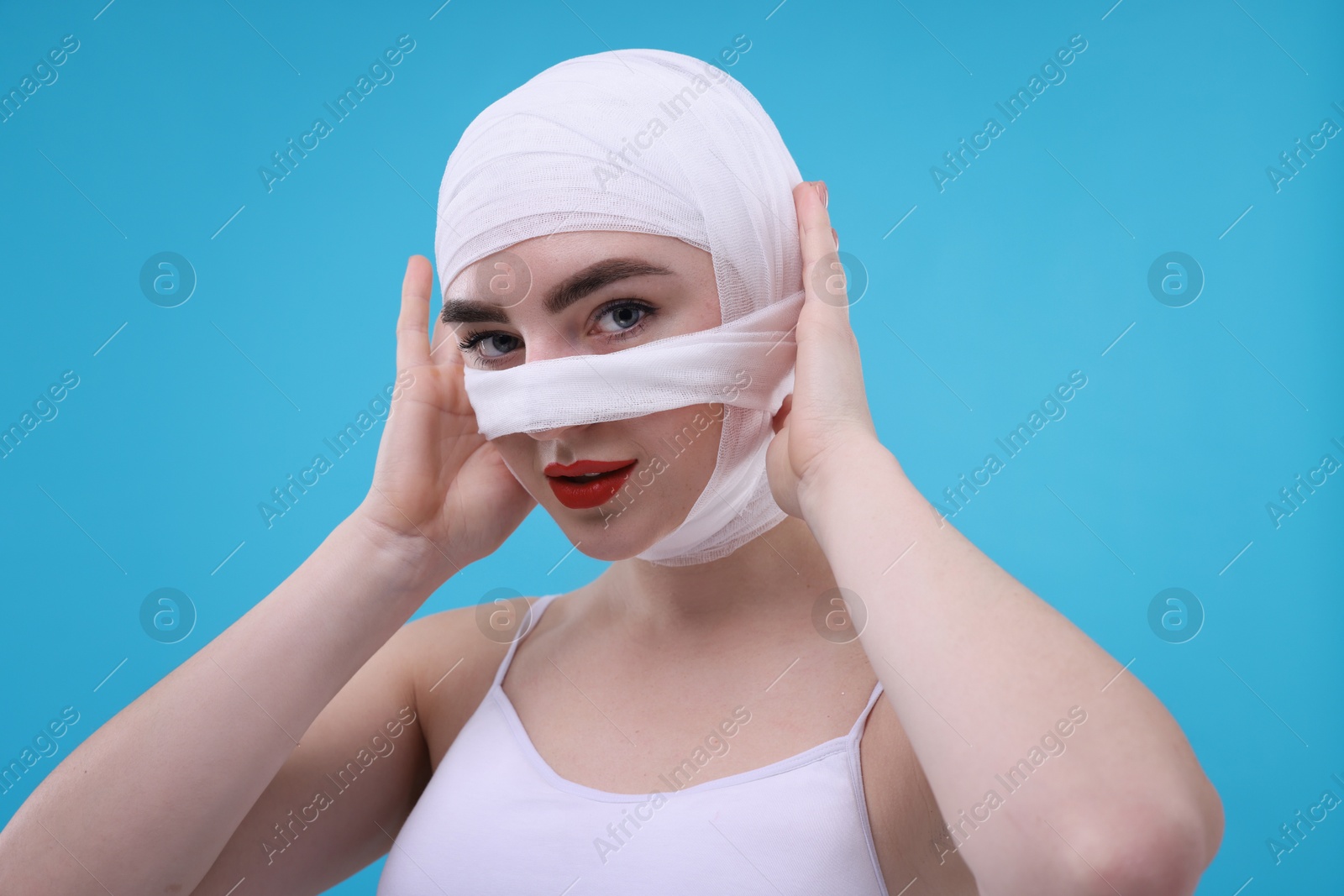 Photo of Woman with nose wrapped in medical bandage after plastic surgery operation on light blue background