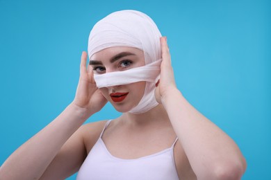 Photo of Woman with nose wrapped in medical bandage after plastic surgery operation on light blue background