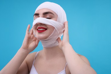 Photo of Woman with nose wrapped in medical bandage after plastic surgery operation on light blue background