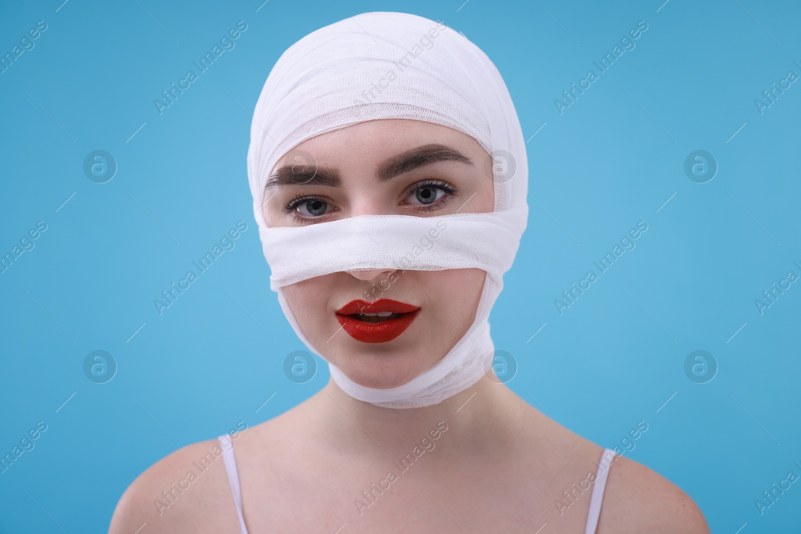 Photo of Woman with nose wrapped in medical bandage after plastic surgery operation on light blue background