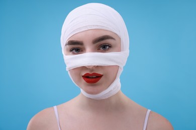 Woman with nose wrapped in medical bandage after plastic surgery operation on light blue background