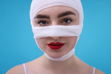 Photo of Woman with nose wrapped in medical bandage after plastic surgery operation on light blue background, closeup