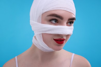 Photo of Woman with nose wrapped in medical bandage after plastic surgery operation on light blue background