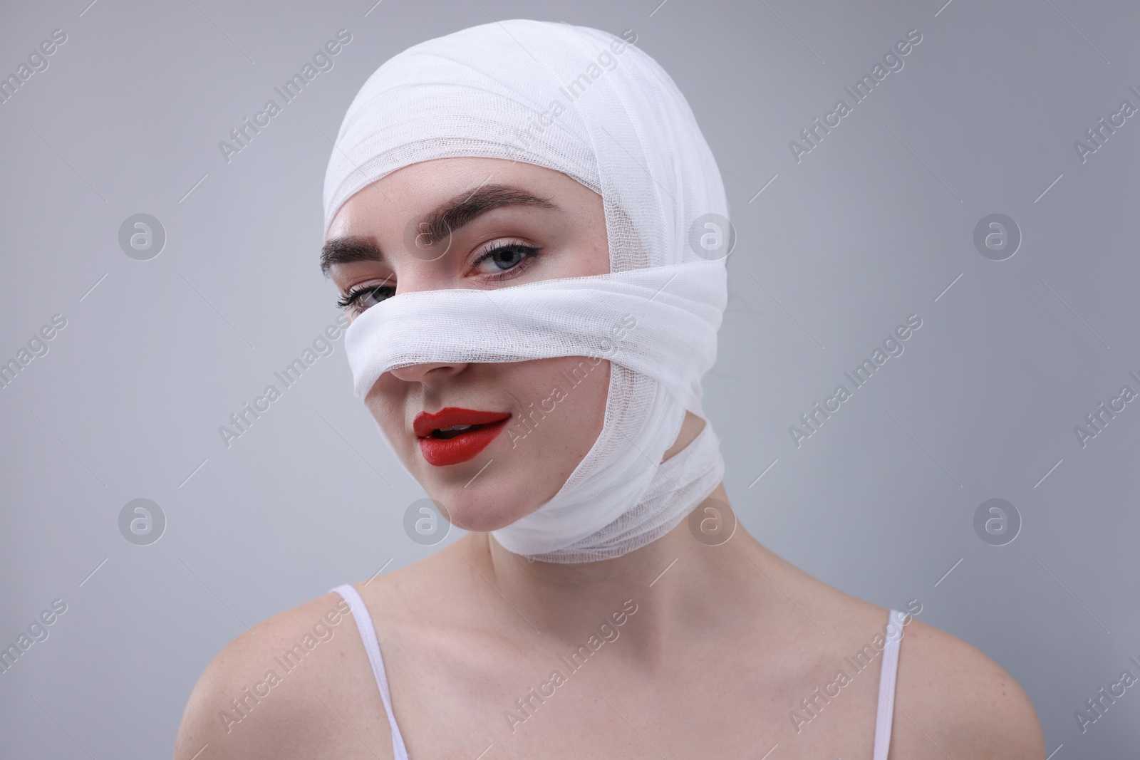 Photo of Woman with nose wrapped in medical bandage after plastic surgery operation on grey background