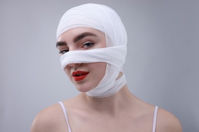 Photo of Woman with nose wrapped in medical bandage after plastic surgery operation on grey background