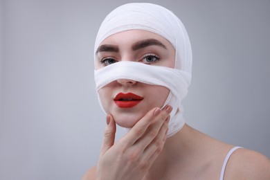 Woman with nose wrapped in medical bandage after plastic surgery operation on grey background, space for text