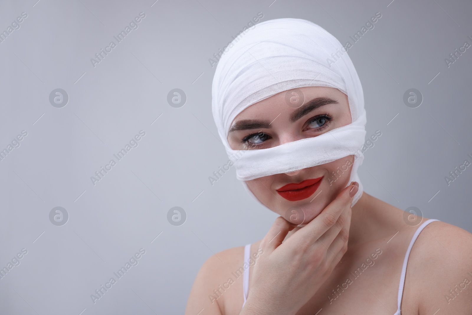 Photo of Woman with nose wrapped in medical bandage after plastic surgery operation on grey background, space for text