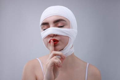 Photo of Woman with nose wrapped in medical bandage after plastic surgery operation making silent gesture on grey background