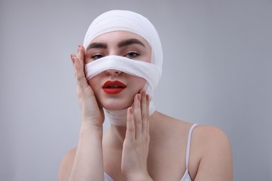 Photo of Woman with nose wrapped in medical bandage after plastic surgery operation on grey background