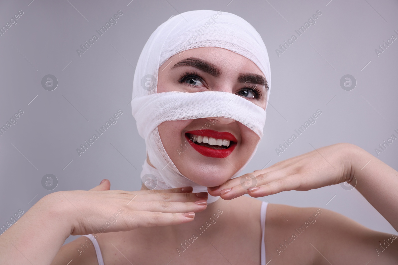 Photo of Woman with nose wrapped in medical bandage after plastic surgery operation on grey background