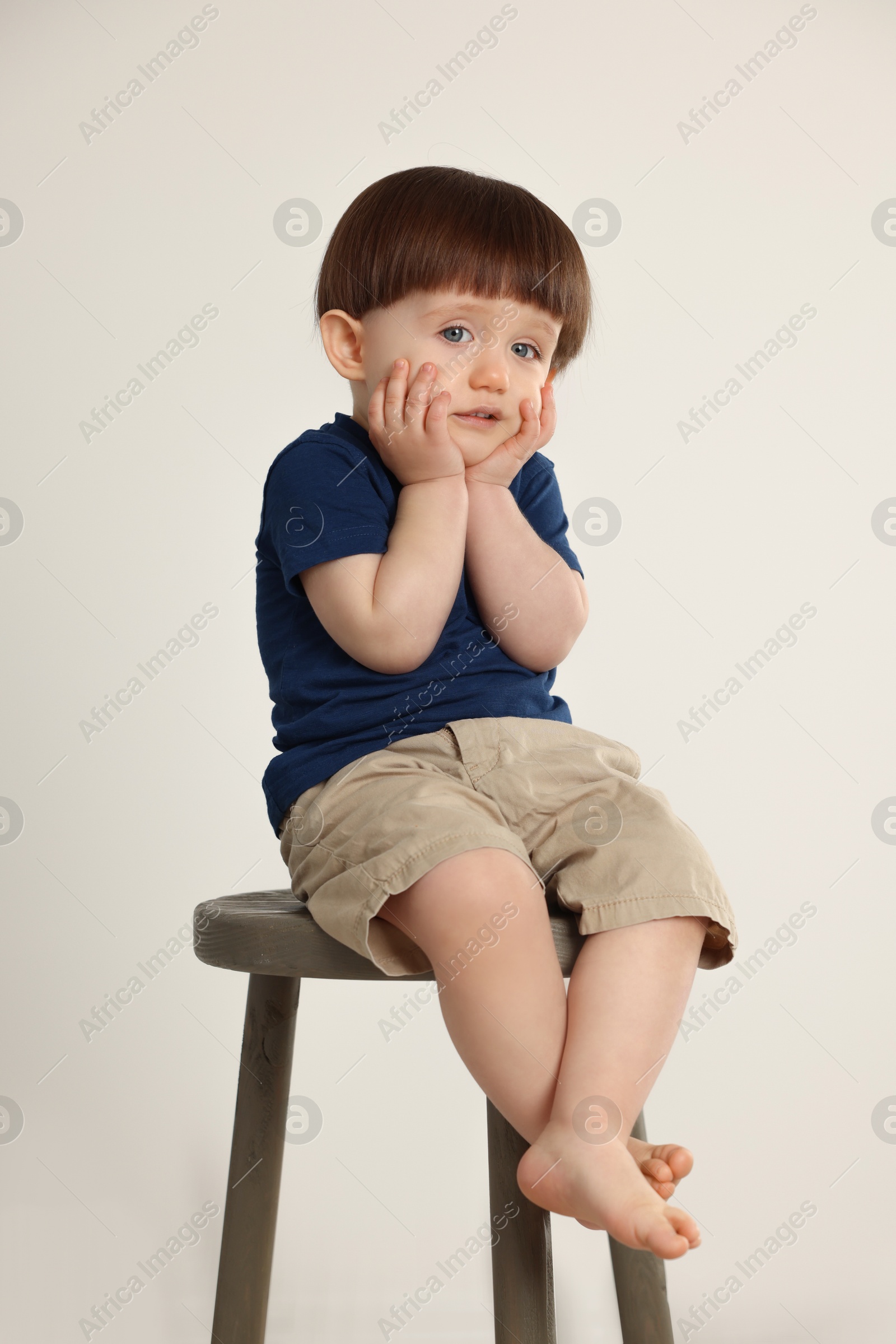 Photo of Cute little boy sitting on stool against light grey background