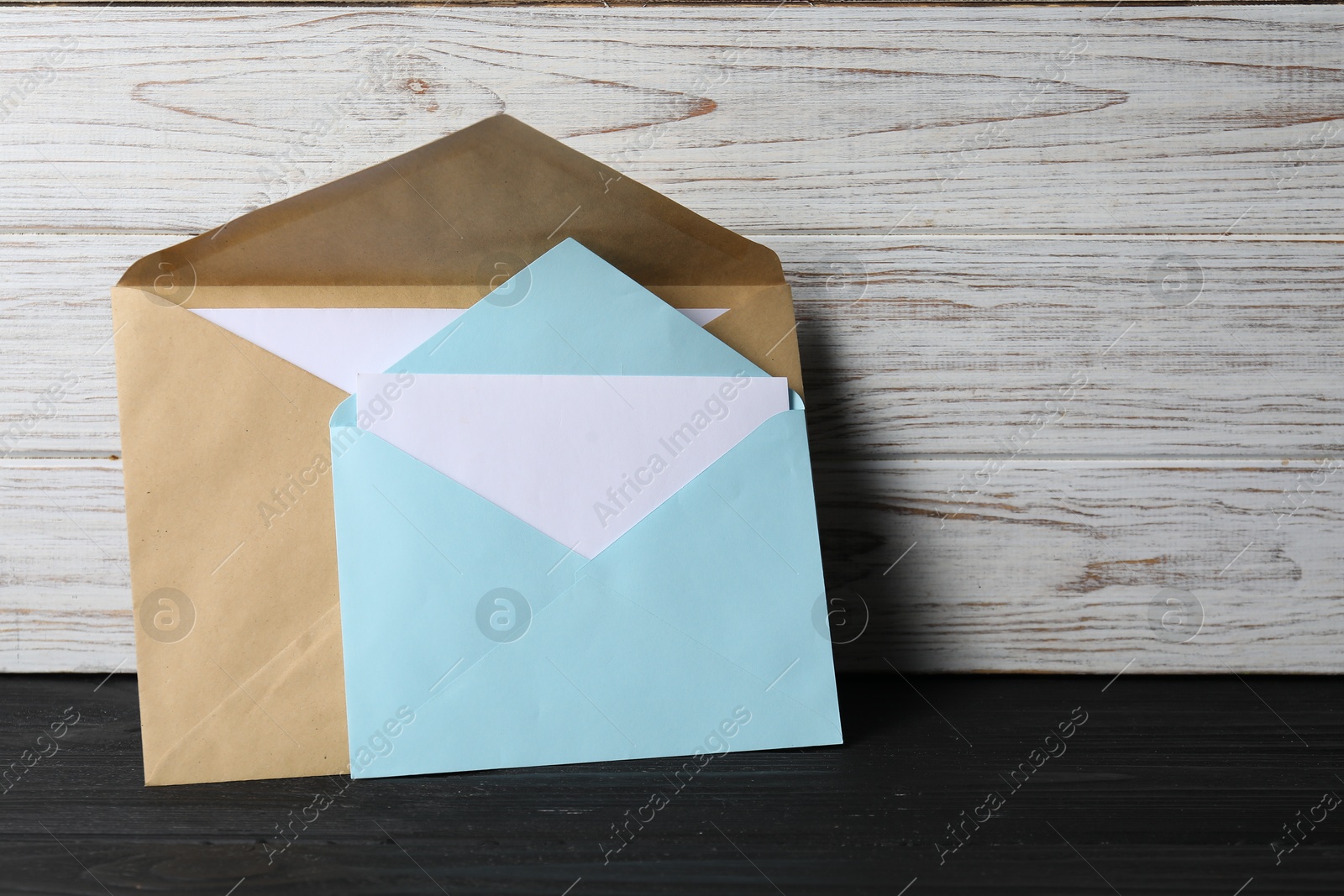 Photo of Paper envelopes with letter on black wooden table. Mockup for design