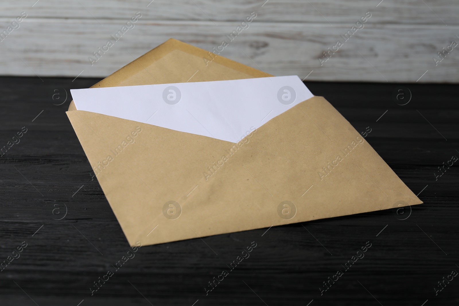 Photo of Kraft paper envelope with letter on black wooden table. Mockup for design