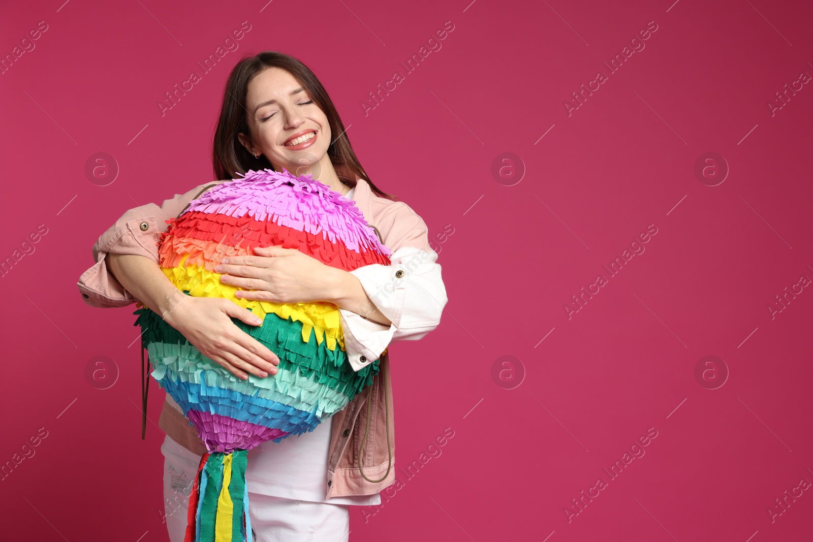 Photo of Happy woman with colorful pinata on pink background, space for text