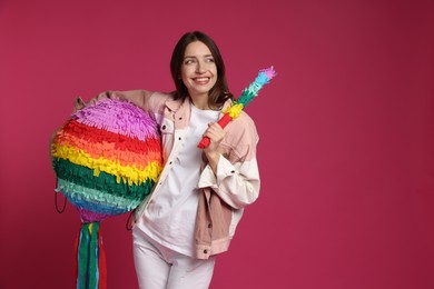 Photo of Happy woman with colorful pinata and stick on pink background, space for text