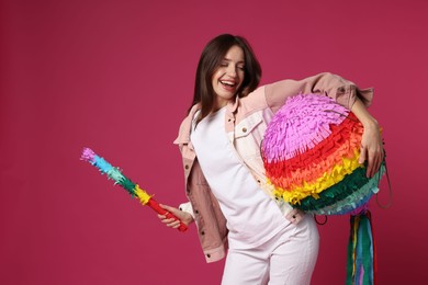 Happy woman with colorful pinata and stick on pink background