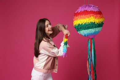 Happy woman breaking colorful pinata with stick on pink background