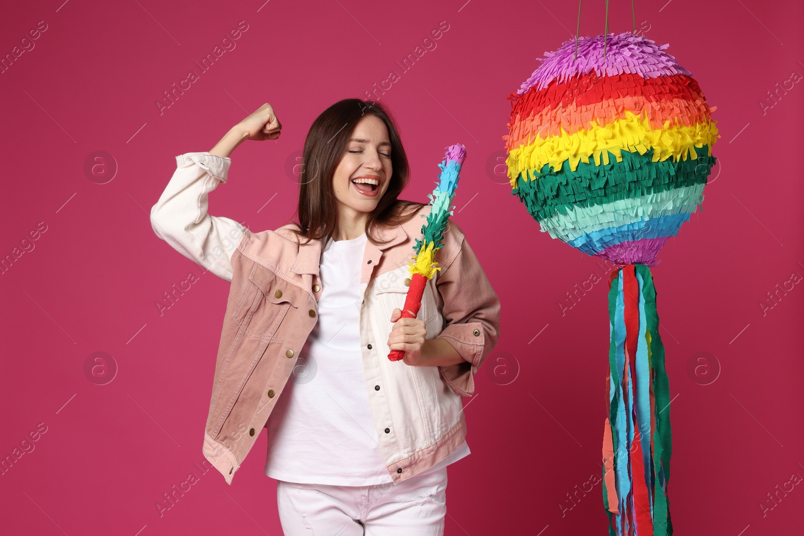 Photo of Happy woman with colorful pinata and stick on pink background