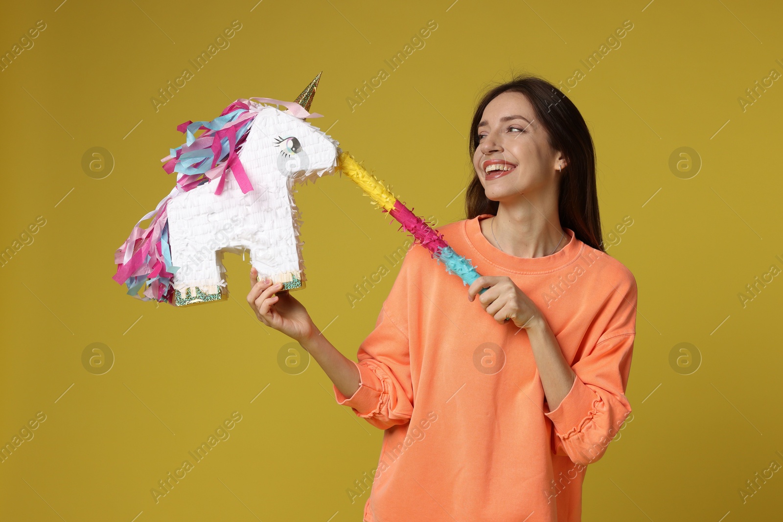 Photo of Happy woman with unicorn shaped pinata and stick on yellow background