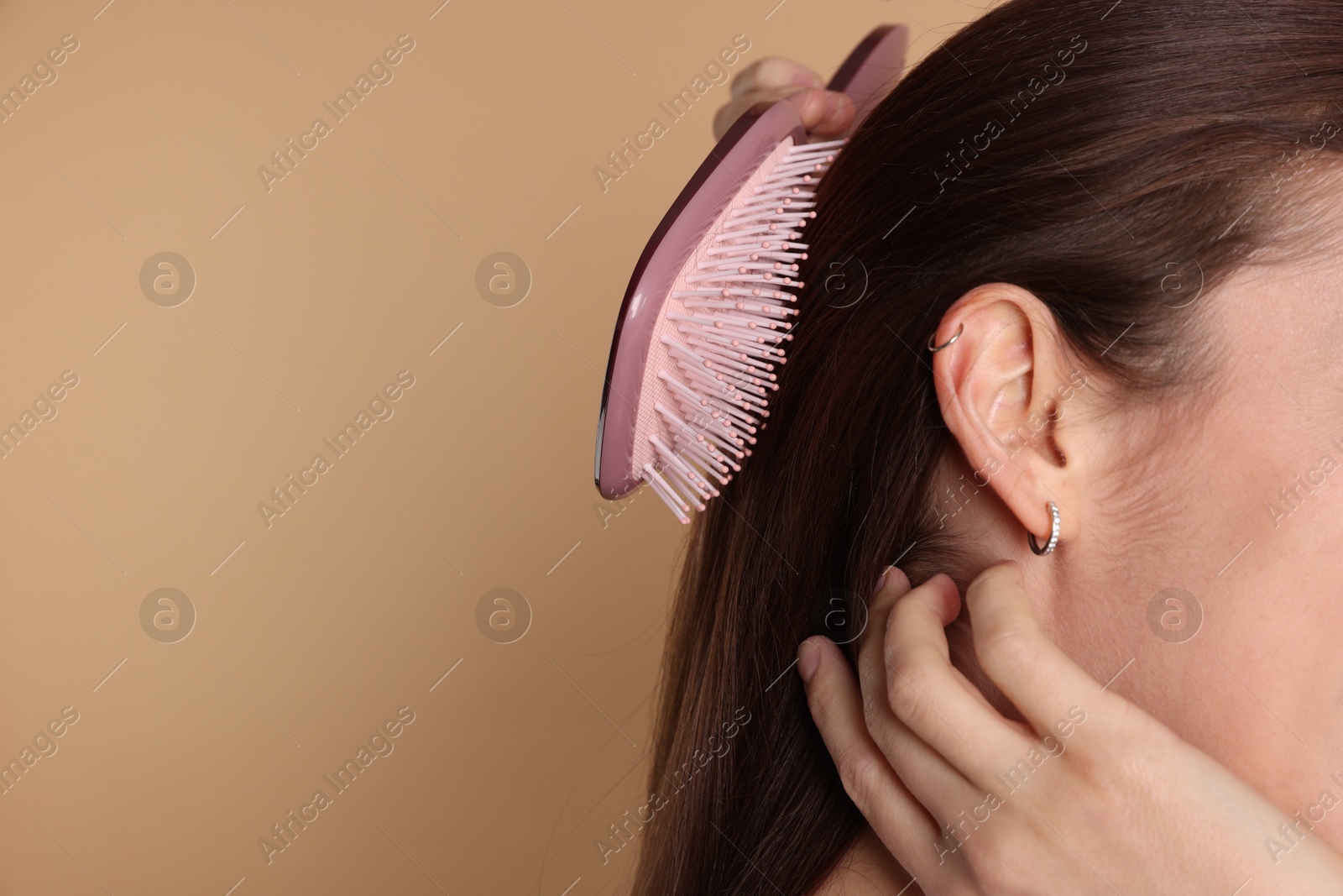 Photo of Woman brushing her hair on beige background, closeup. Space for text