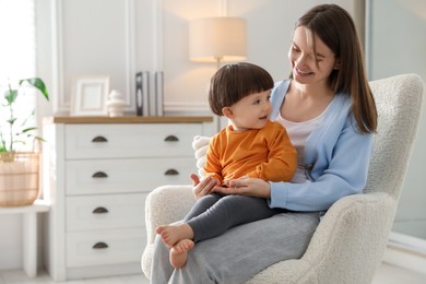 Photo of Happy mother with her little son sitting on armchair at home. Space for text