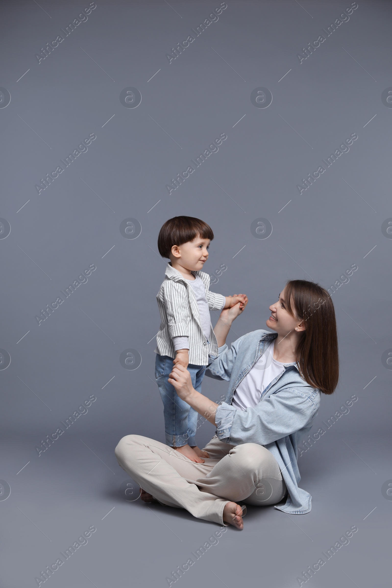 Photo of Happy mother with her little son on grey background. Space for text