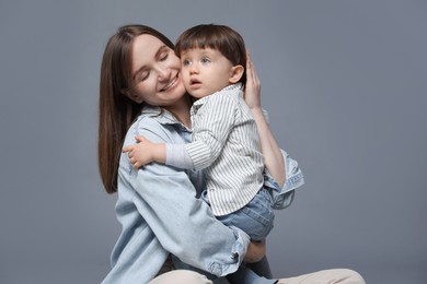 Photo of Happy mother hugging her little son on grey background