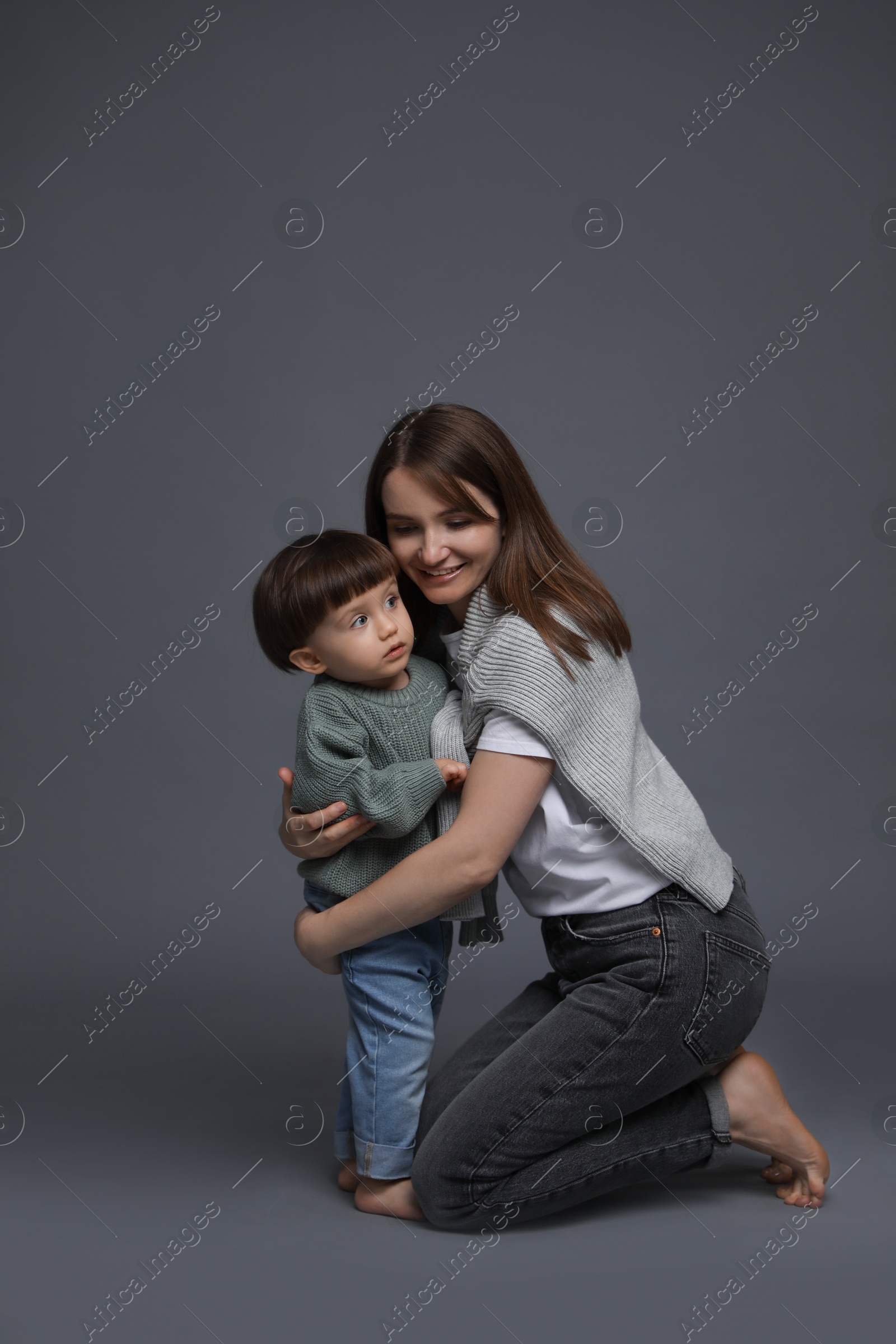 Photo of Happy mother hugging her little son on grey background