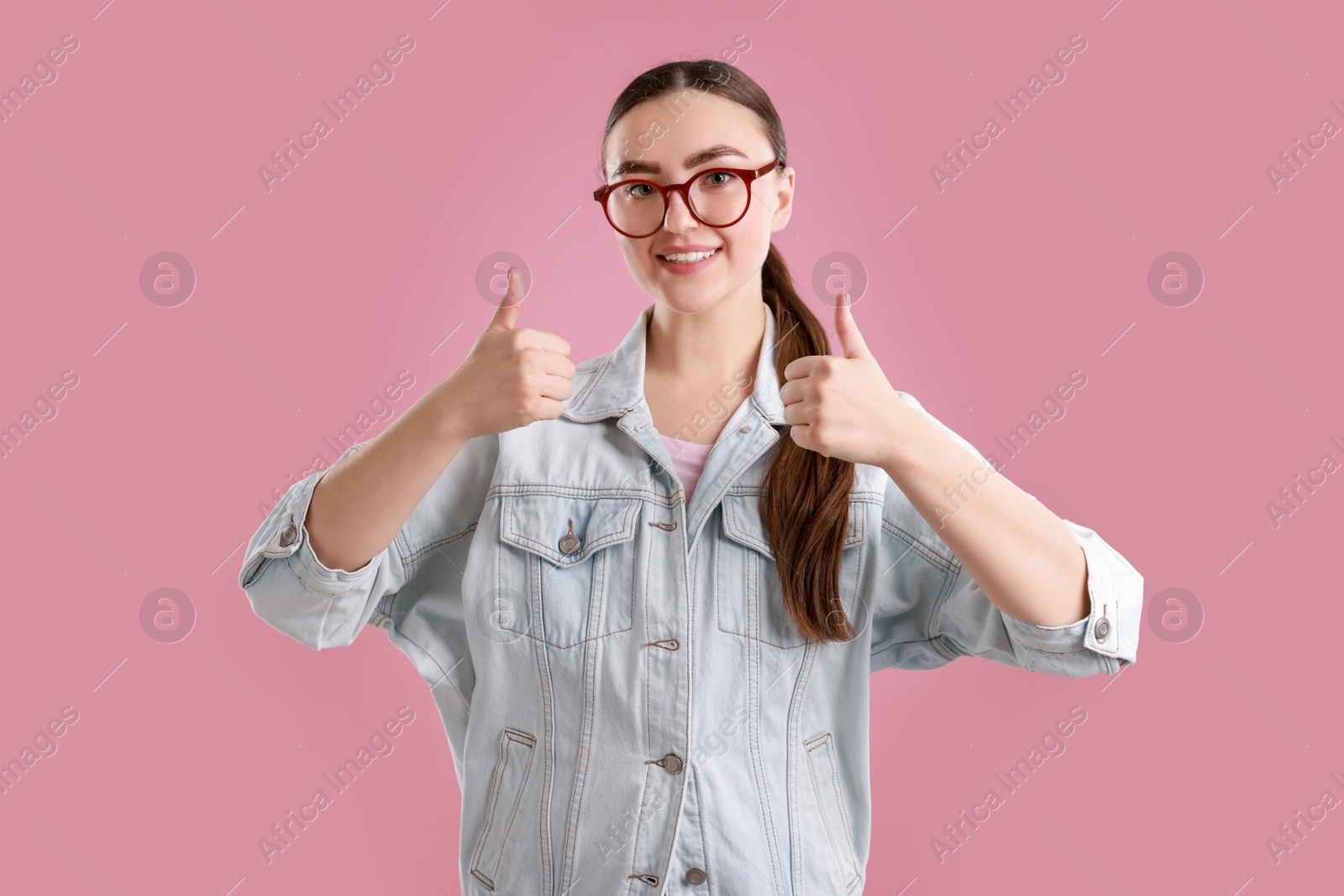 Photo of Happy woman showing thumbs up on pink background. Like gesture