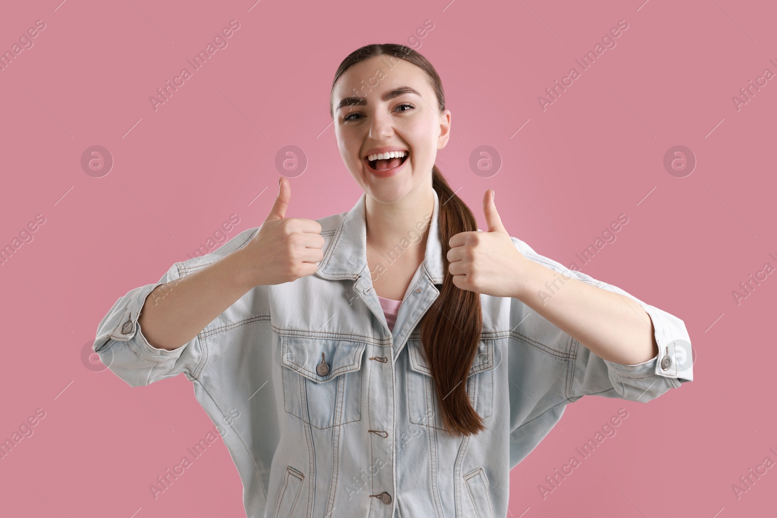 Photo of Happy woman showing thumbs up on pink background. Like gesture