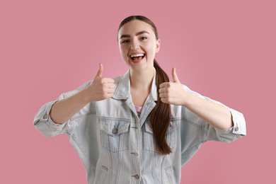 Photo of Happy woman showing thumbs up on pink background. Like gesture