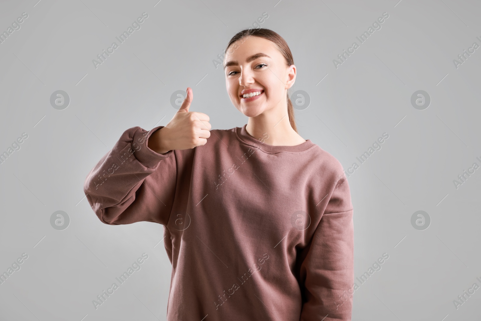 Photo of Happy woman showing thumbs up on grey background. Like gesture