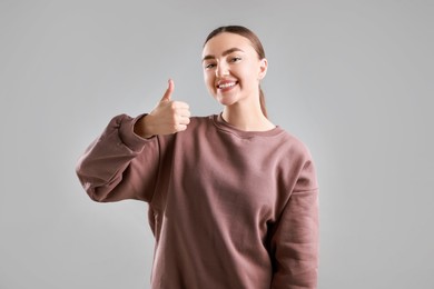 Photo of Happy woman showing thumbs up on grey background. Like gesture