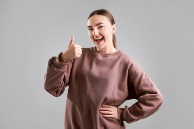 Photo of Happy woman showing thumbs up on grey background. Like gesture