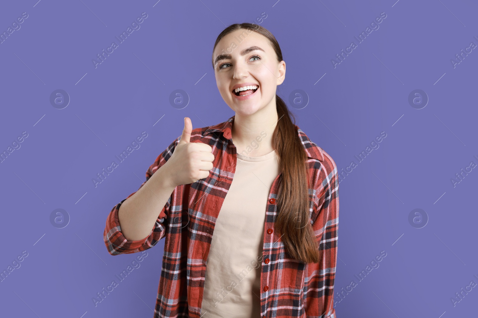 Photo of Happy woman showing thumbs up on purple background. Like gesture