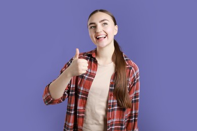 Photo of Happy woman showing thumbs up on purple background. Like gesture